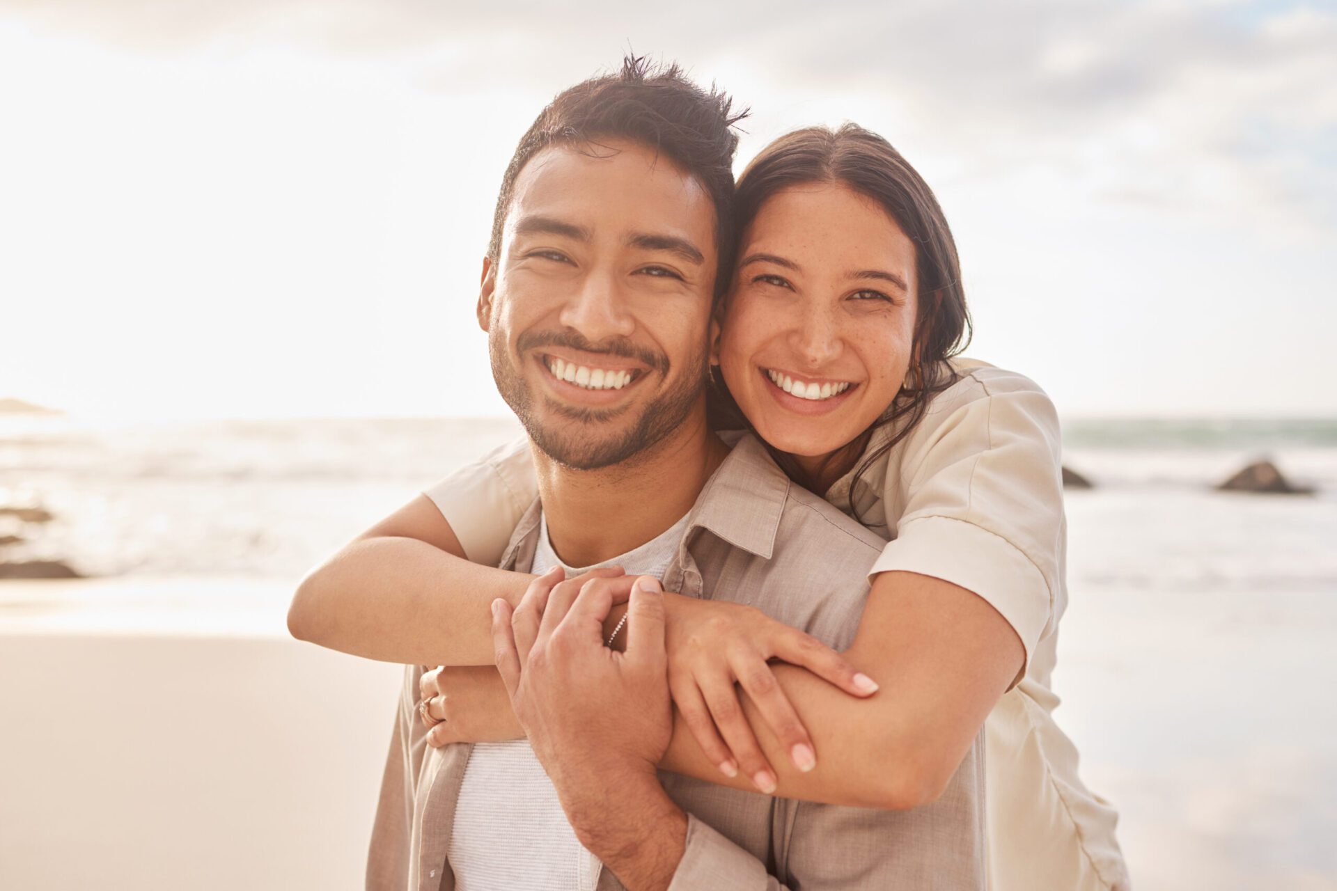 Portrait, hug and couple at the beach with happiness for a vacation in the summer having fun. Together, hugs and ocean for holiday with smile for the weekend with sunshine for relaxing and bonding. dentist in lakewood
